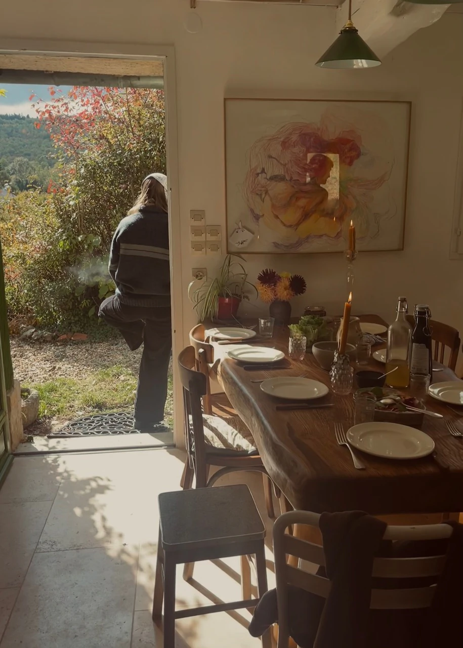 Table dressée dans la cuisine de la ferme, avec vue sur le jardin et une personne sortant par la porte